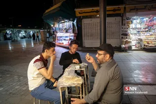 حضور تعدادی از مجاوران روزه‌دار و مغازه داران اطراف حرم مطهر، همزمان با اذان مغرب و لحظه افطار در نزدیکی حرم حضرت معصومه (س)