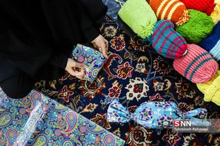 یکی از اعضای گروه جهادی شهیدان رستمی در حال کادو کردن  شال و گردن های بافته شده می باشد.